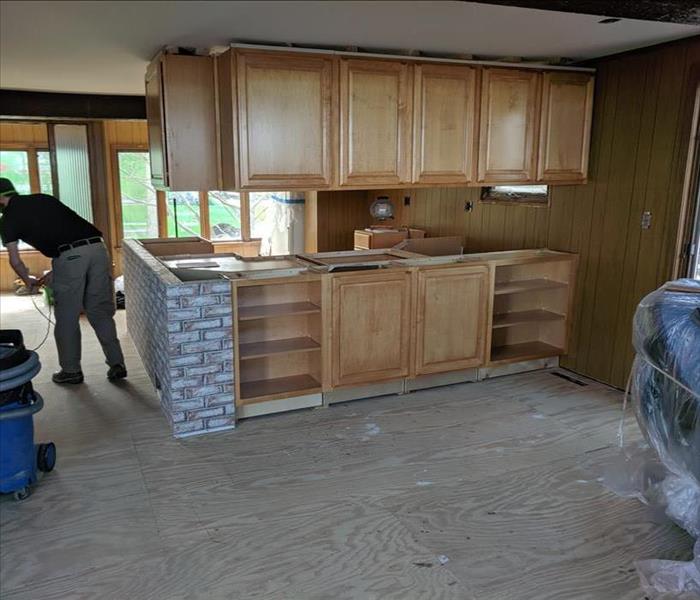 A restored kitchen with new wooden cabinets and decorative tile, as well as a new plywood floor, plus a technician.
