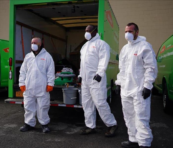 Three SERVPRO employees in Tyvek and face masks preparing to disinfect a building.