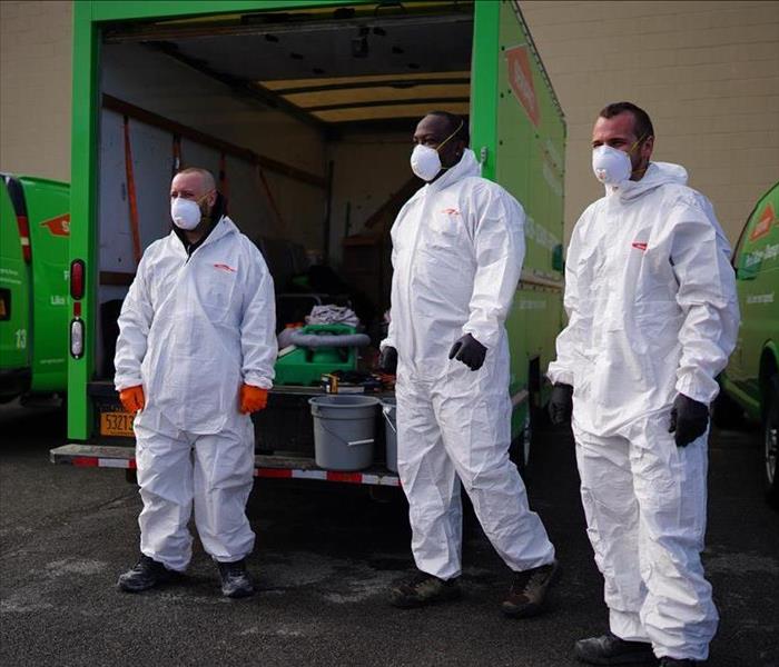3 male SERVPRO technicians in TYVEK next to a SERVPRO truck preparing to disinfect a business.