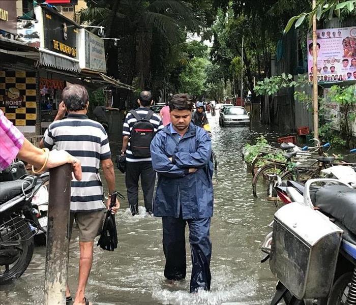 Man frowning with arms crossed looking down in a flooded city street.