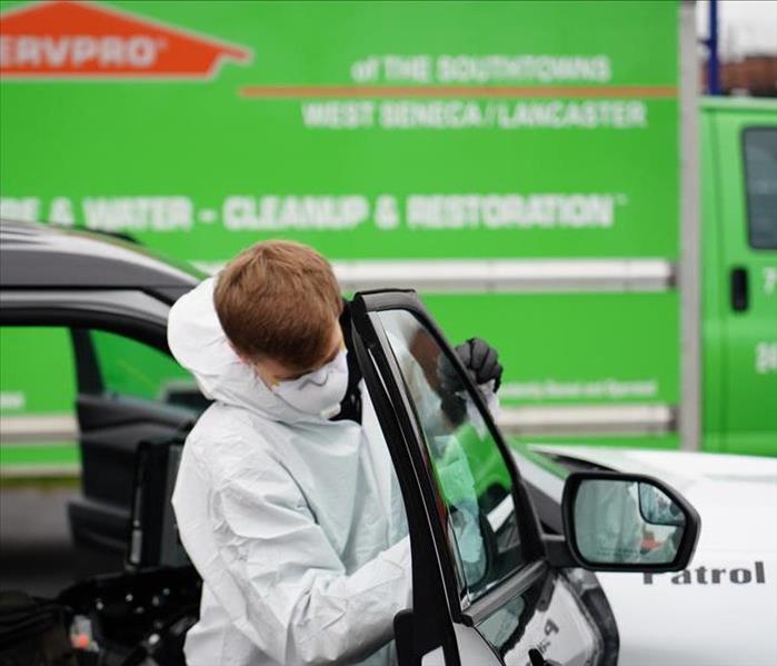 SERVPRO technician in Tyvek cleaning the glass in the backseat of a police car.